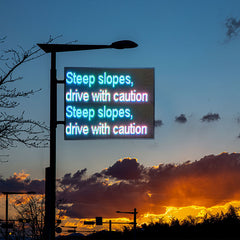 Electronic sign warning of steep slopes with a sunset in the background