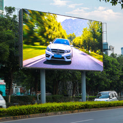 Digital billboard displaying a car on a scenic road with trees and mountains in the background.