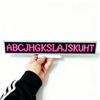 Hand holding a small LED display board with pink letters on a white background