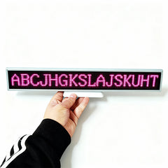 Hand holding a small LED display board with pink letters on a white background