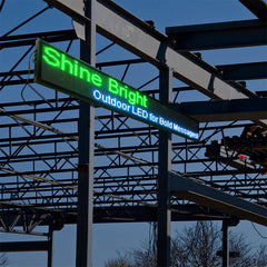 Green LED sign on a metal structure against a blue sky