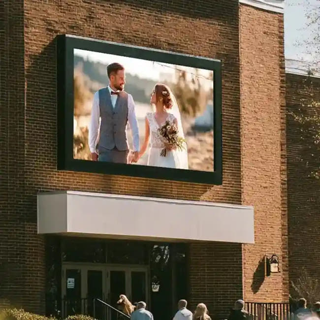 Digital display showing a bride and groom on a brick building exterior. Main image