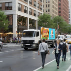 White truck with a colorful advertisement on a city street with pedestrians and buildings.