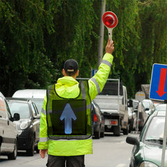 Person in a high-visibility vest directing traffic with a red light signal.
