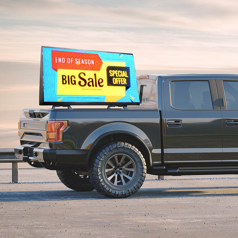 Gray pickup truck with a digital display showing a sale advertisement on a road.