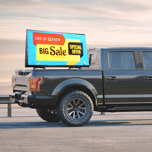 Gray pickup truck with a digital display showing a sale advertisement on a road.
