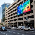 Multistory building with a large digital billboard displaying colorful graphics and text, with cars and pedestrians on the street below.