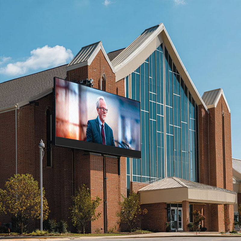Large digital display on a brick building showing a person, with a clear blue sky in the background.