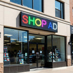 Storefront with a colorful LED sign displaying 'SHOP AD' above glass doors.