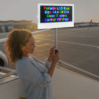 Woman holding a portable LED sign with text on an airport tarmac.