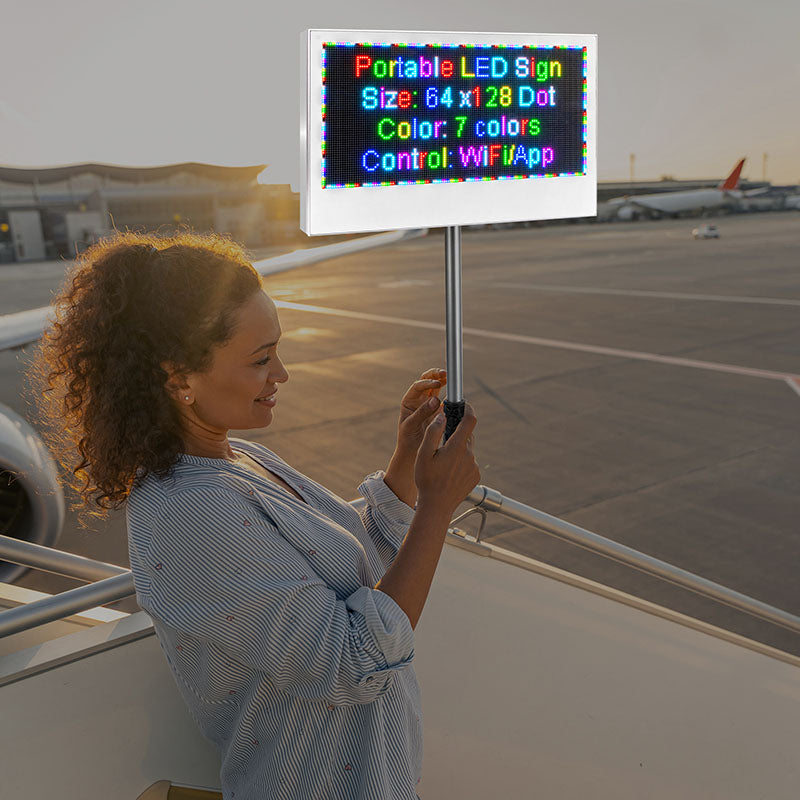 Woman holding a portable LED sign with text on an airport tarmac.
